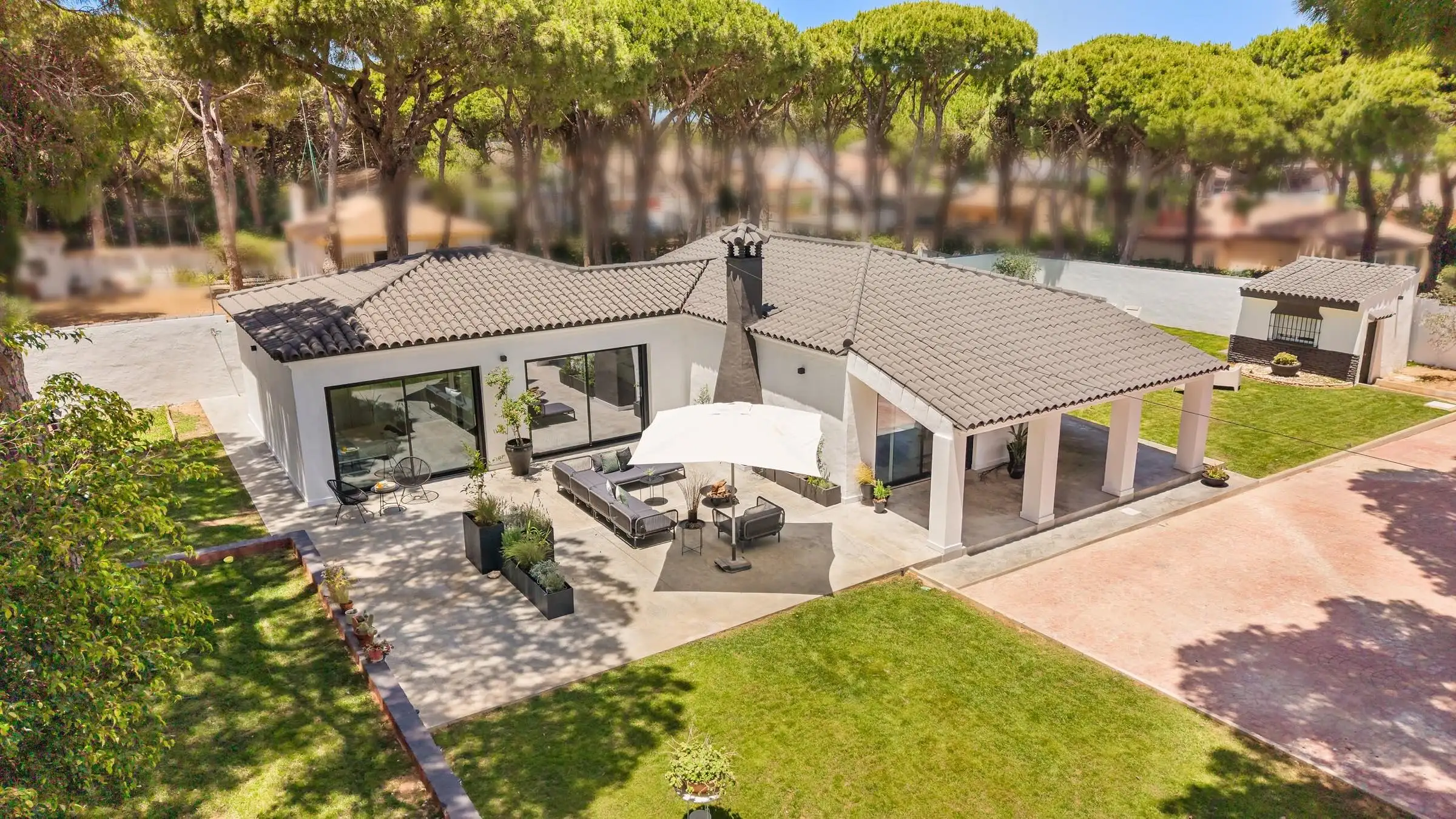 Villa Juju von oben: weiße eingeschossige Villa mit Ziegeldach, beschatteter Terrasse und Rasen im Schirmpinienwald.